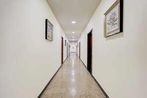 A corridor with framed artwork on the walls, doors leading to rooms, and a marble floor. - Townhouse JFN Comfort Hotel (Chennai)