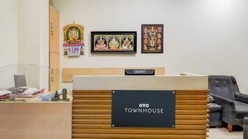 A reception desk with a sign reading 'OYO TOWNHOUSE', a wooden desk, a black chair, and framed religious artwork on the wall.