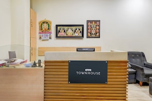 A reception desk with a sign reading 'OYO TOWNHOUSE', a wooden desk, a black chair, and framed religious artwork on the wall. - Townhouse JFN Comfort Hotel (Chennai)
