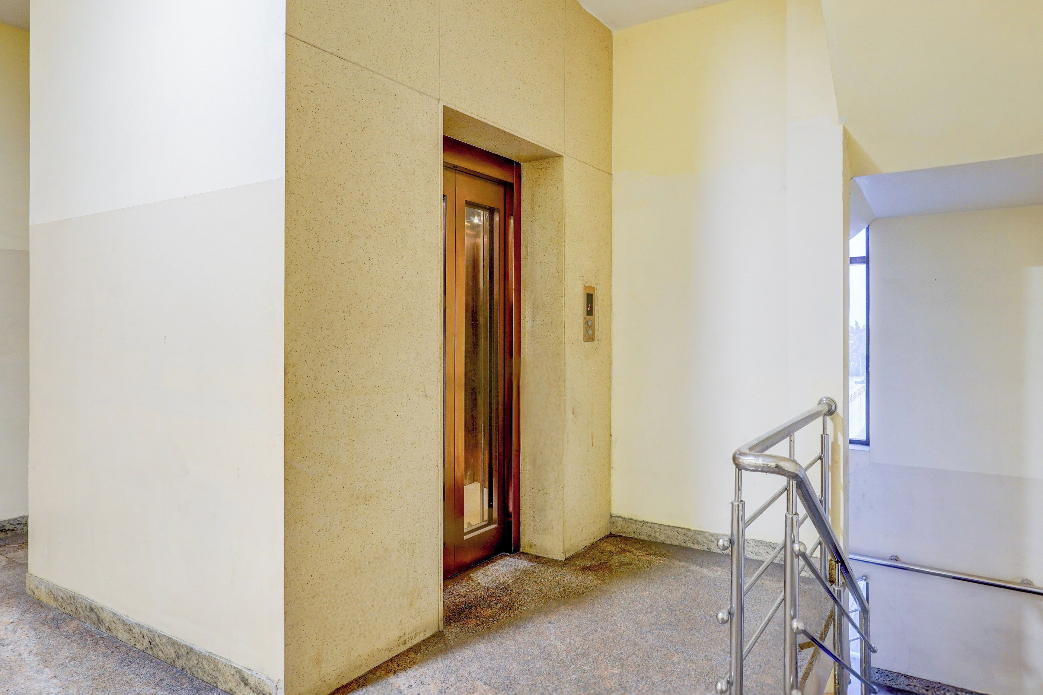 A hallway with a door leading to an elevator, a handrail, and a marble floor.