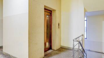 A hallway with a door leading to an elevator, a handrail, and a marble floor.