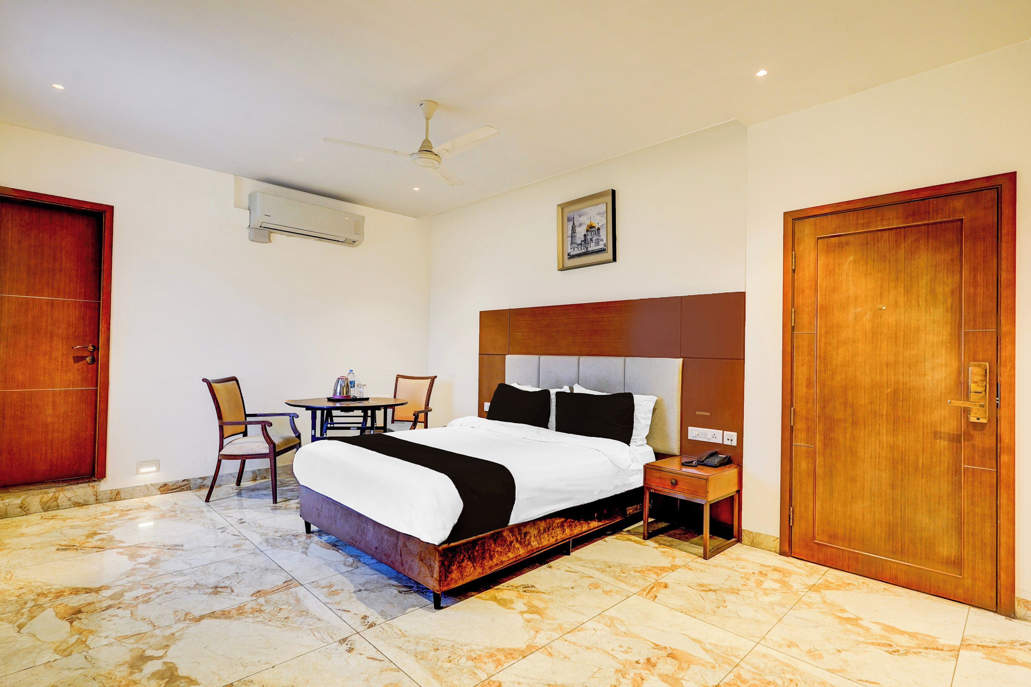 A hotel room with a bed, a desk, a chair, a table, and a ceiling fan.
