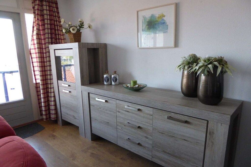 A room with a grey cabinet, a window with curtains, a framed artwork on the wall, and two potted plants.
