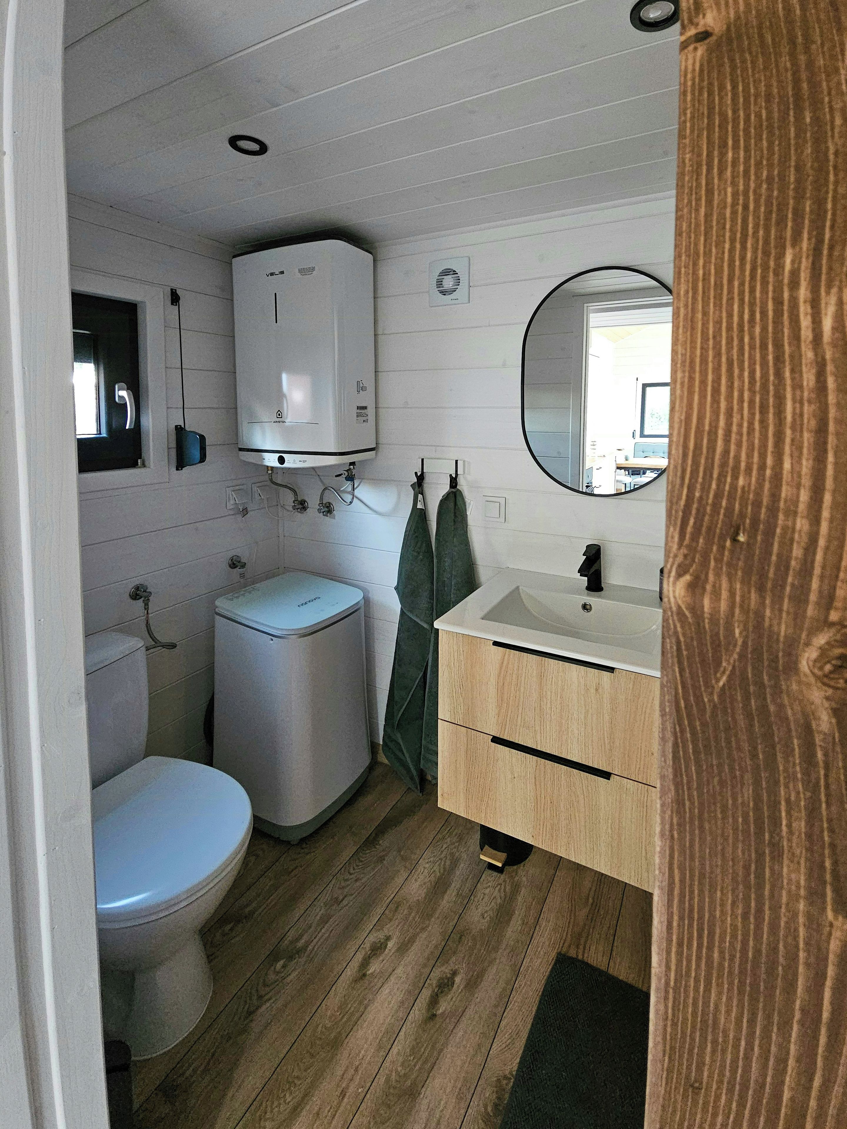 A compact bathroom with a toilet, a washing machine, a sink, and a mirror.