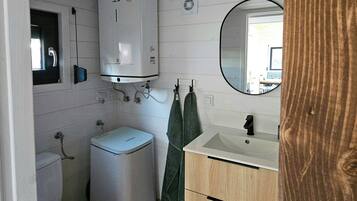 A compact bathroom with a toilet, a washing machine, a sink, and a mirror.