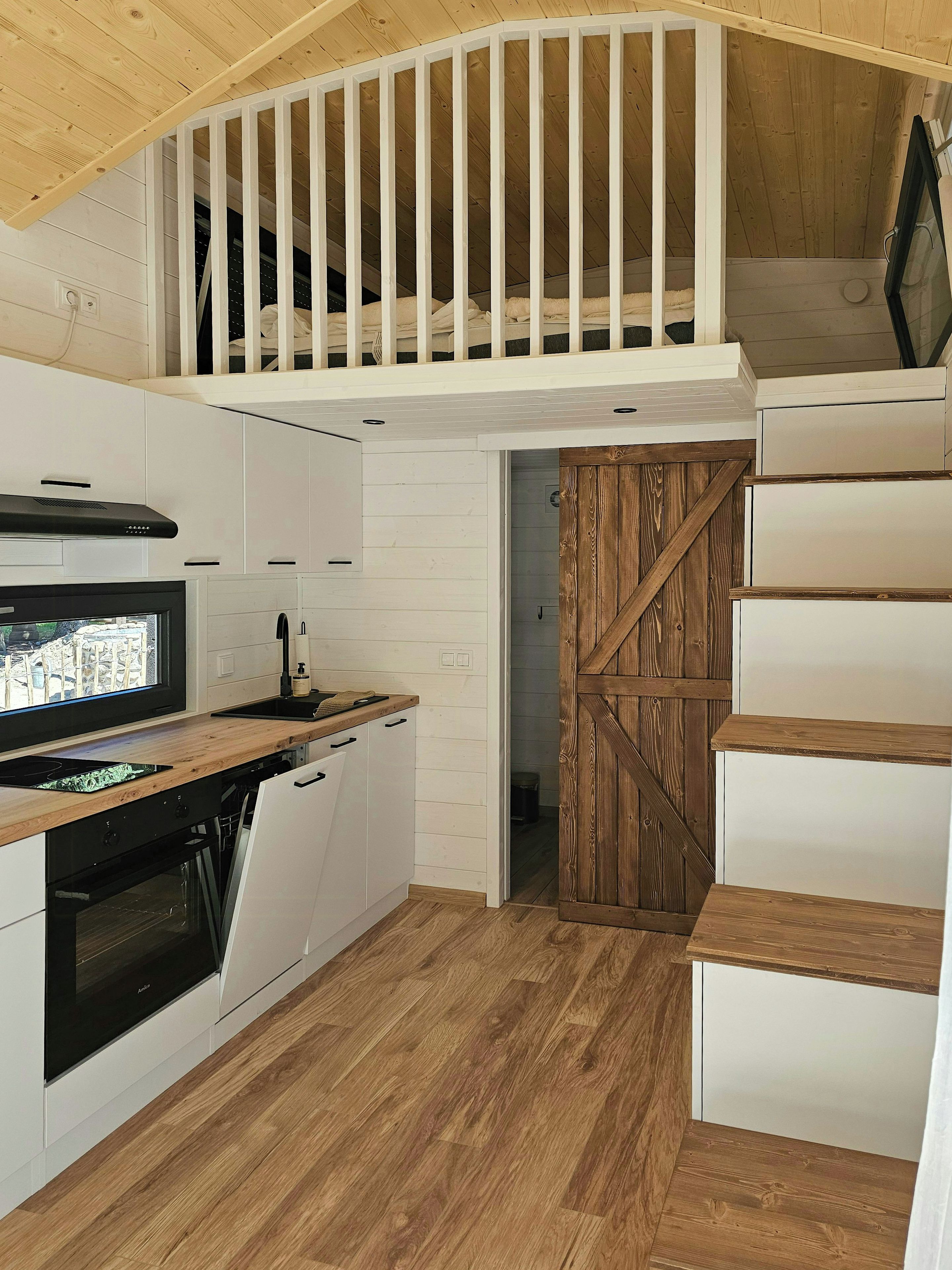 Een kleine keuken met een houten plafond, witte keukenkastjes en een ingebouwde oven.