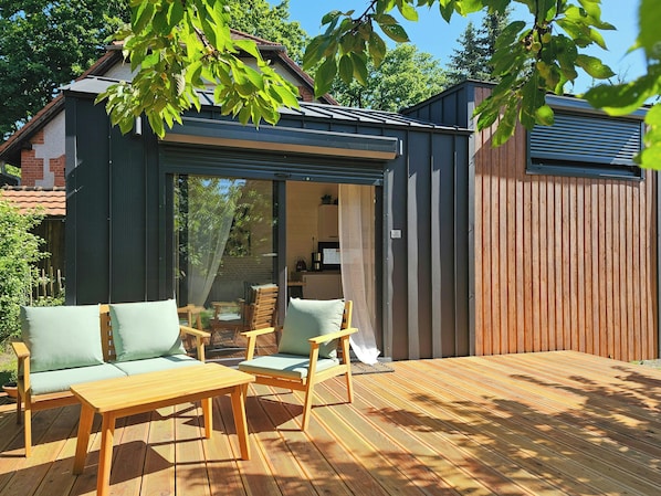 Ein moderner Außenbereich mit Holzterrasse, einer glasgeschlossenen Veranda und Blick auf die umliegende Natur.