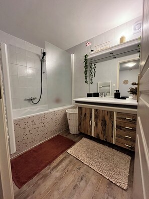 Un baño con ducha, lavabo, espejo y un cesto de basura.
