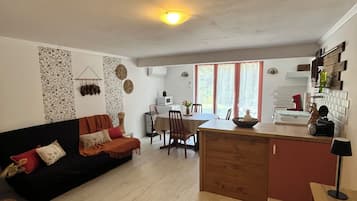 A living room with a sofa, a dining table with chairs, a kitchen area with a counter, and a wooden cabinet.