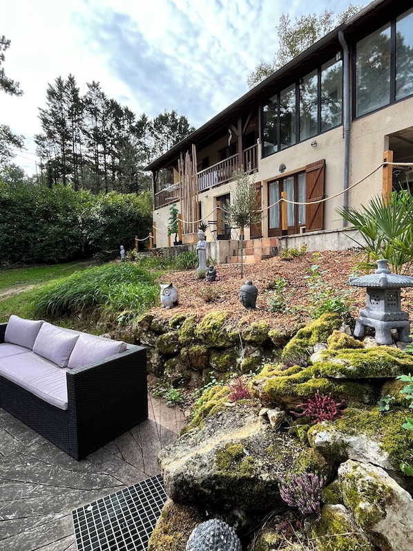 Una casa moderna con balcón, un sendero de piedra y un jardín con rocas cubiertas de musgo y una estatua de Buda.