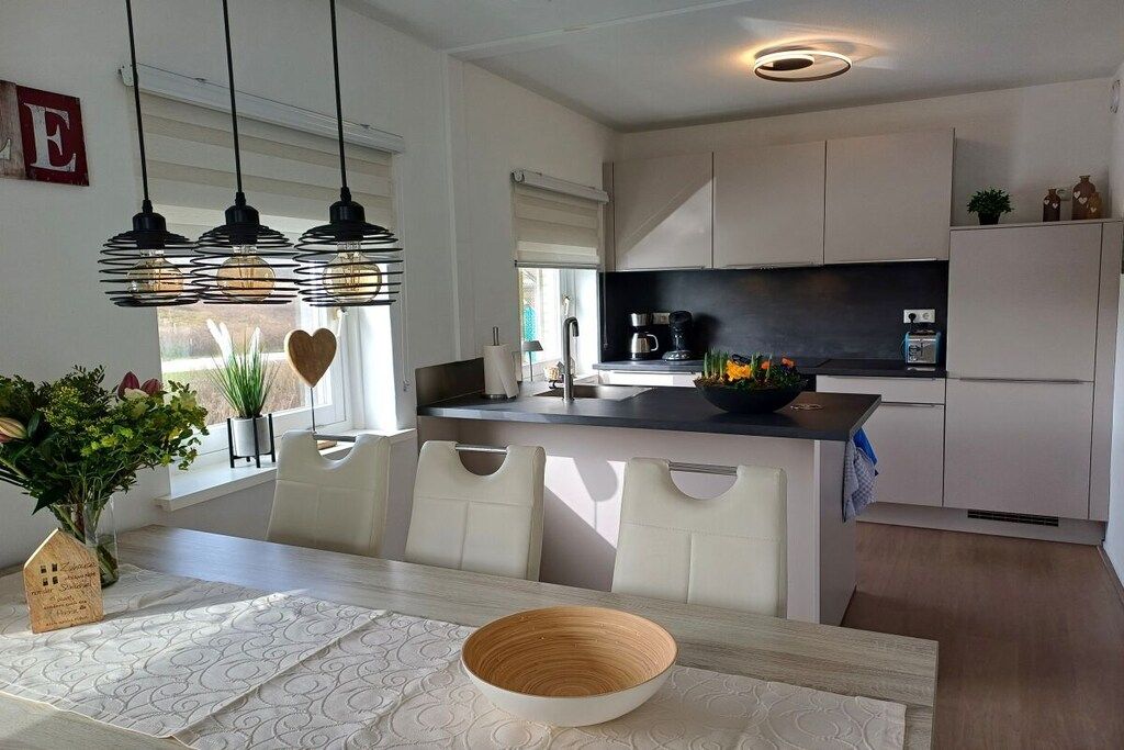 A modern kitchen with a central island, pendant lighting, and a dining area with a table and chairs.