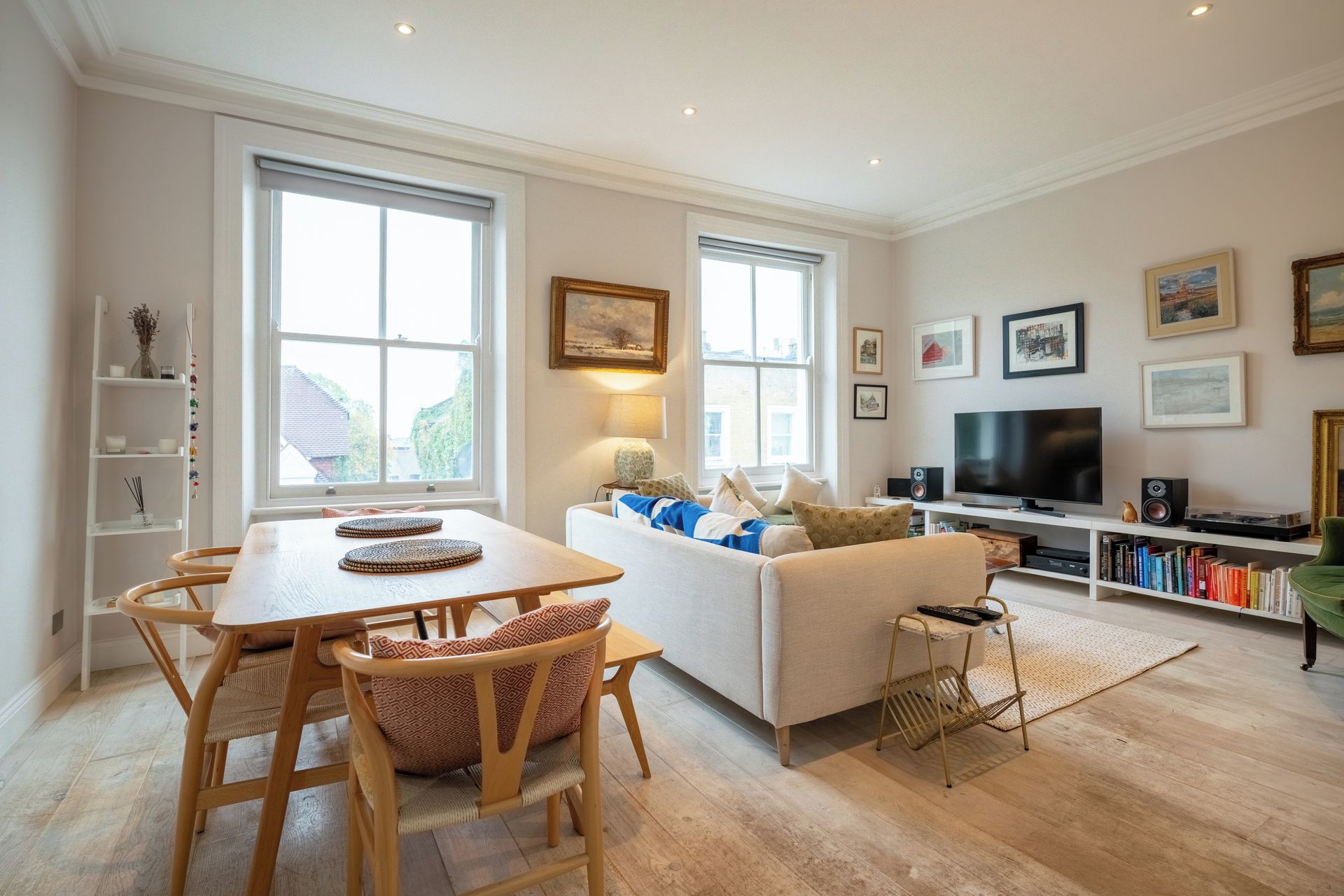 A modern living room with a sofa, a dining table with chairs, a TV, and a bookshelf.