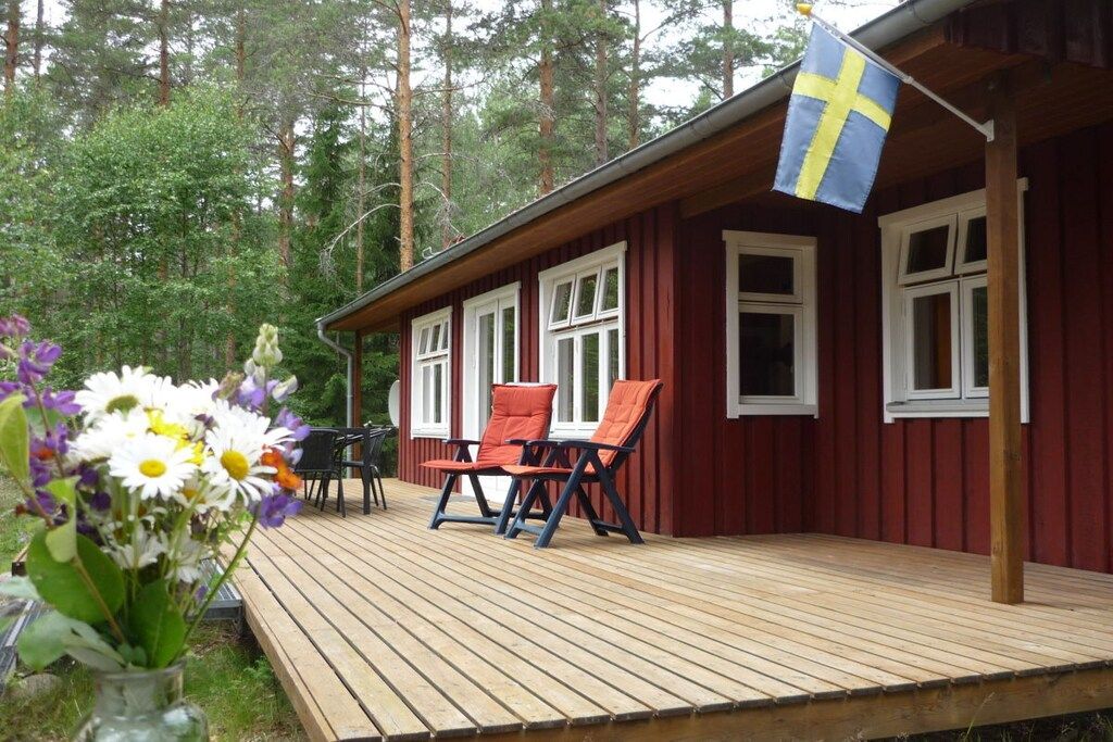 Eine Holzterrasse mit zwei Stühlen, einem Tisch, einer Flagge und einem bewaldeten Hintergrund.