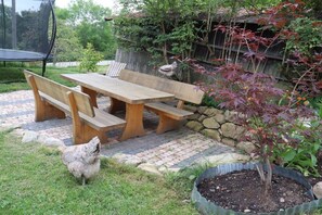Een houten picknicktafel met banken, een stenen muur, een kip en een bloempot.