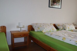Een eenpersoonsbed met een bloemenbedekker, een nachtkastje met een lamp, en een aan de muur hangend schilderij.