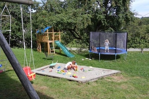 Ein Spielplatz mit Rutsche, Schaukeln, Trampolin und einem Spielbereich mit Spielzeug.