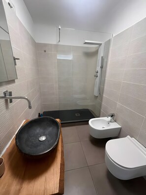 Un baño con un lavamanos negro tipo recipiente, un lavamanos blanco sobre pedestal y un inodoro.