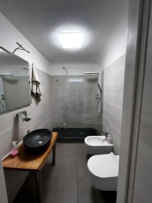 Un baño moderno con un lavabo negro, inodoro blanco y cabina de ducha con mampara de vidrio.