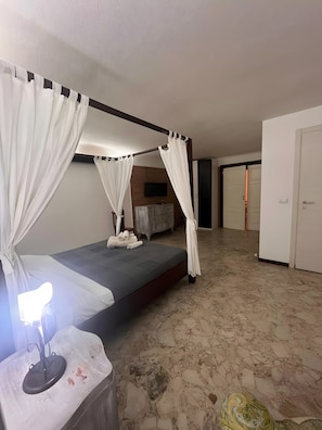 Una habitación con una cama, una mesita de noche con lámpara, un armario y un televisor en la pared.