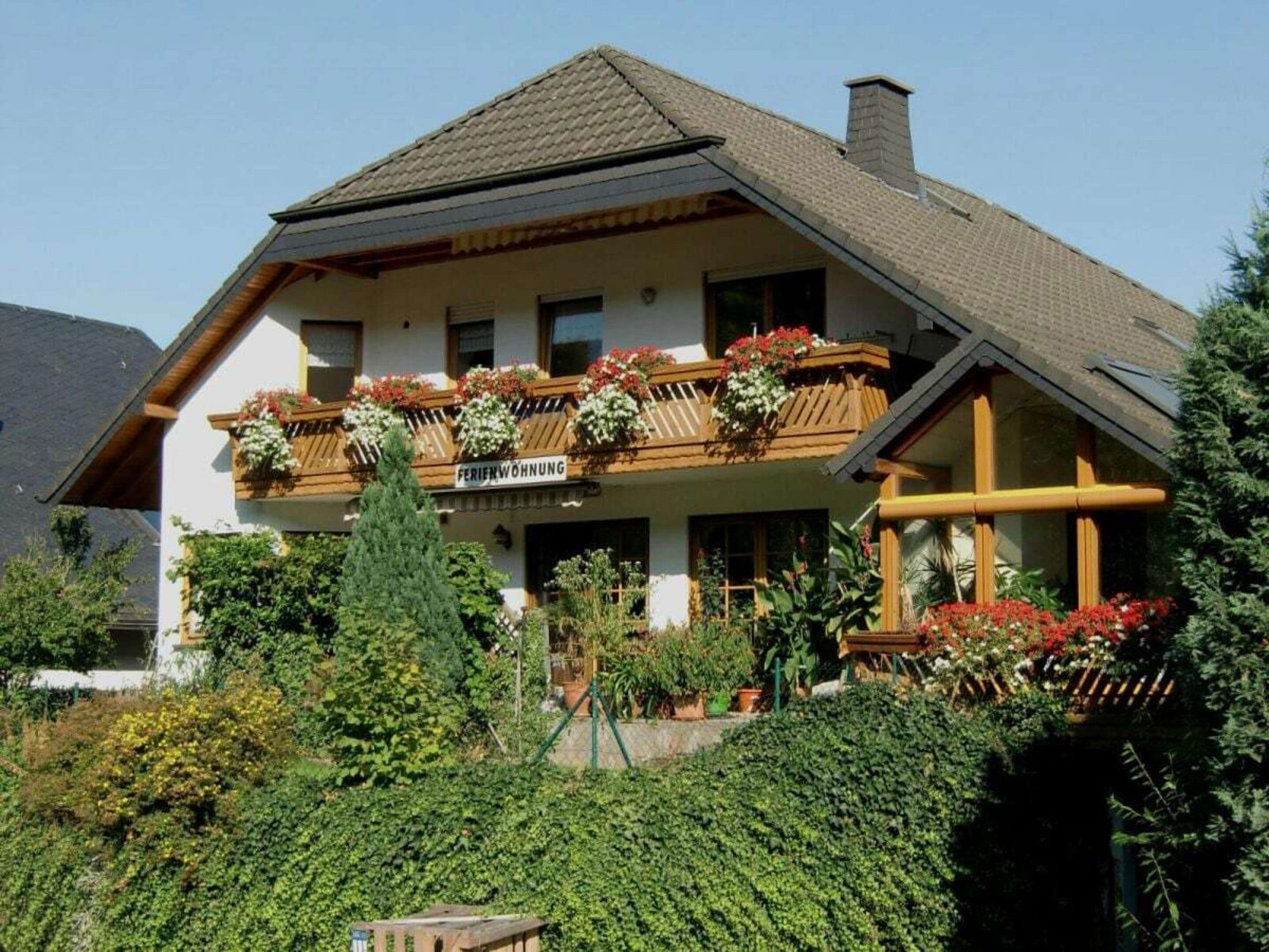 A two-story building with a balcony, surrounded by greenery.