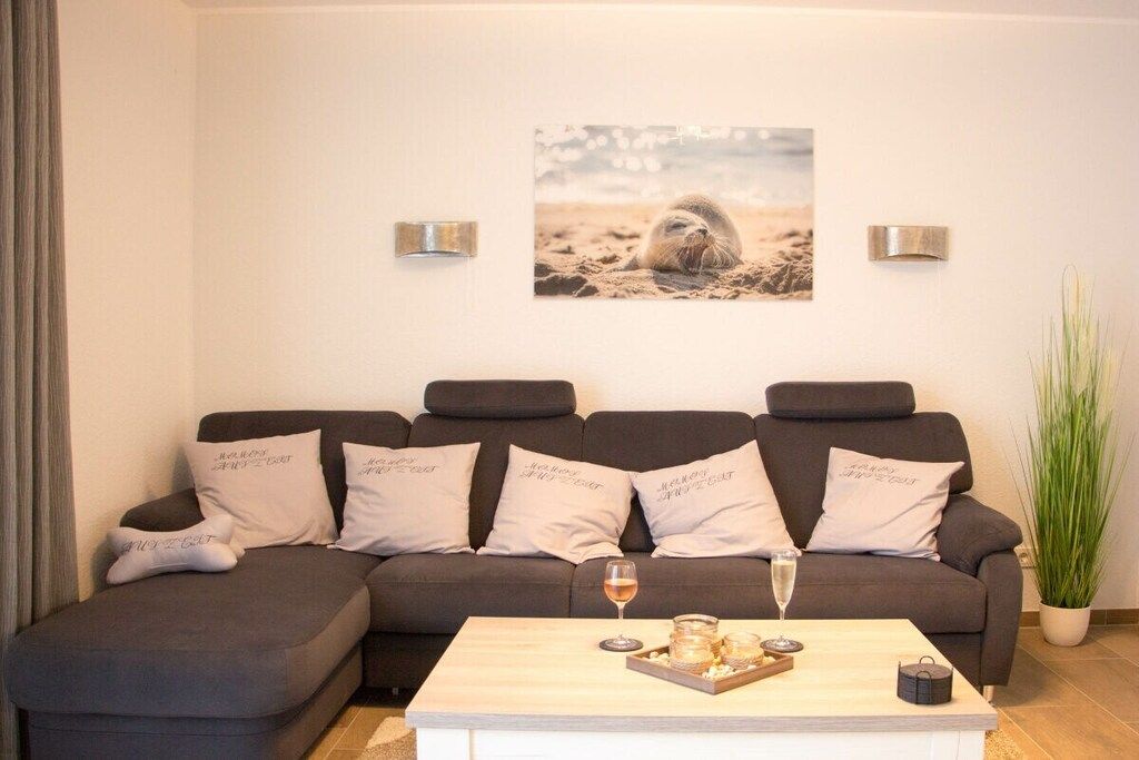 A modern living room with a sectional sofa, a coffee table with a glass and candle, and a wall-mounted picture of a seal on the beach.