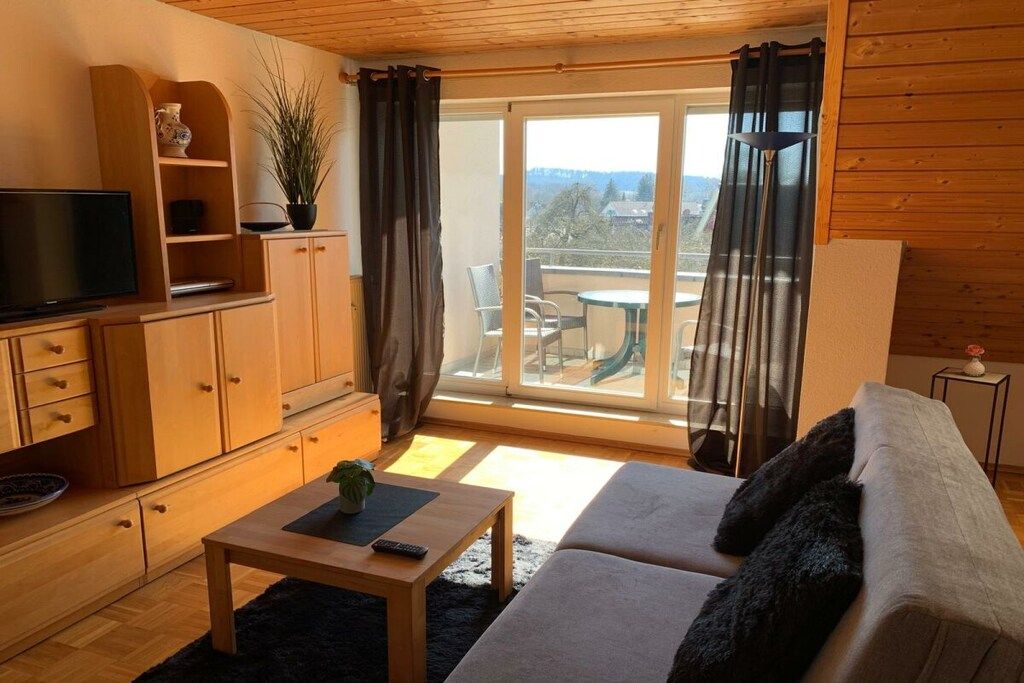 A furnished living room with a sofa, a coffee table, a TV, and a sliding glass door leading to an outdoor area.
