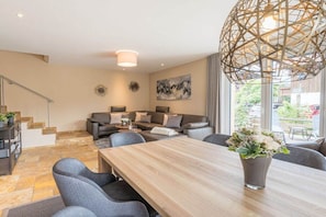 A modern living room with a dining table, grey sofas, and a large window with a view.