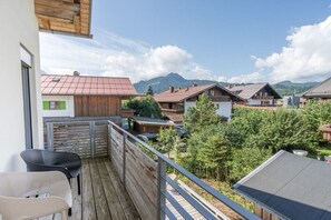 A balcony with wooden railings overlooking a village with traditional houses and a mountain in the background.