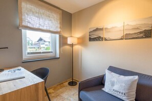 A room with a window, a lamp, a sofa, and a table with a cushion.