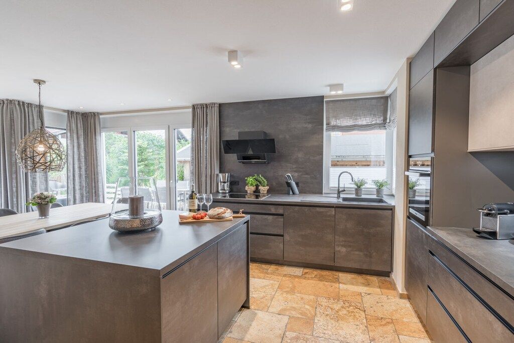 A modern kitchen with a central island, dark cabinetry, and a built-in oven.