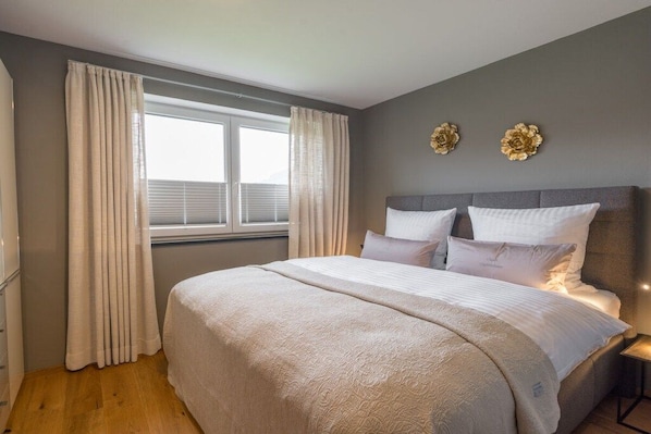A bedroom with a large bed, curtains, a window, and decorative wall art.