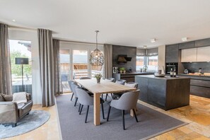 A modern kitchen with a central island, dining area with chairs, and a large window.