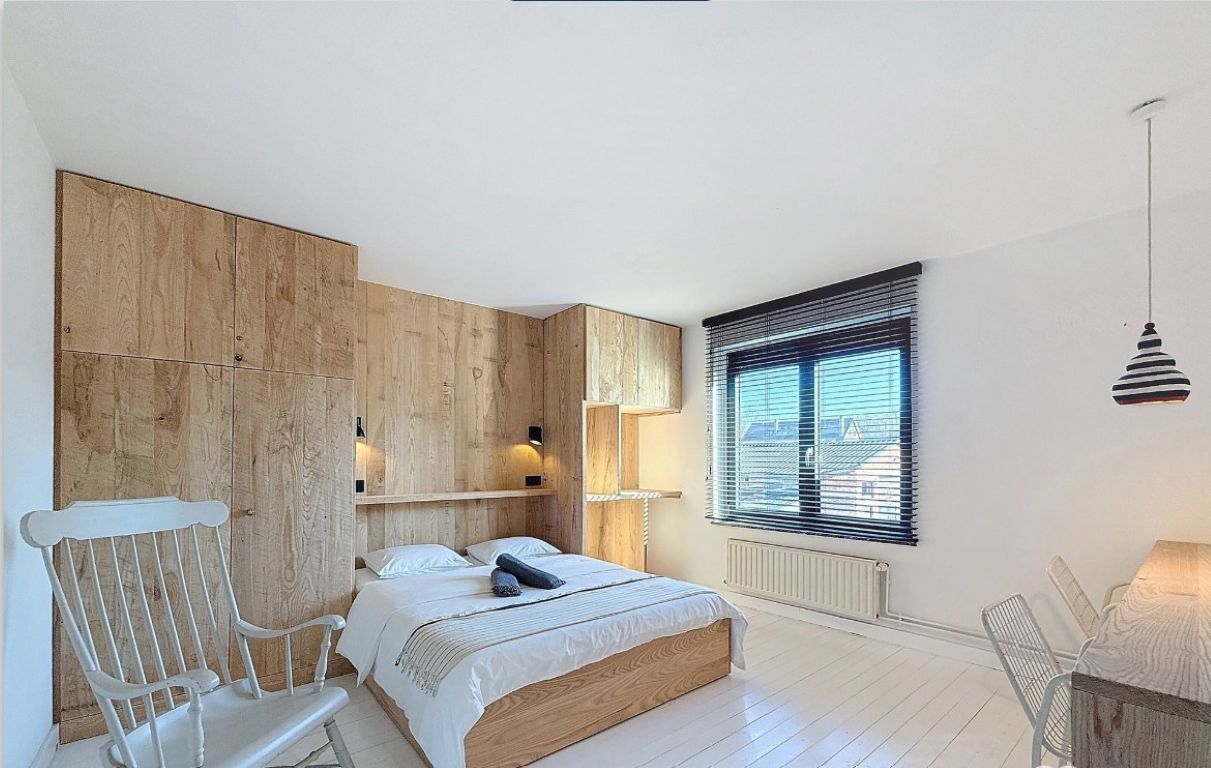 Een slaapkamer met een bed, een stoel, een raam met zonwering en een hanglamp.