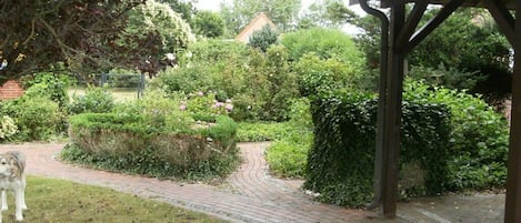 A garden pathway with a gazebo structure, surrounded by lush greenery and a brick path.