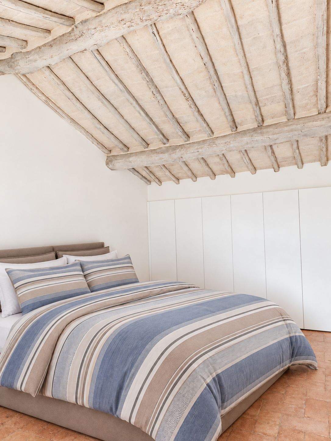 Ein Schlafzimmer mit Holzboden, einem Bett mit gestreifter Bettwäsche und weißem Wandverkleidung.
