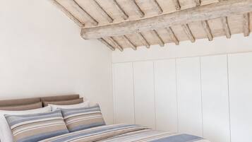 Ein Schlafzimmer mit Holzboden, einem Bett mit gestreifter Bettwäsche und weißem Wandverkleidung.