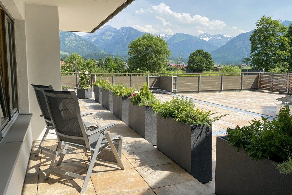 An outdoor seating area with chairs and planters, overlooking a mountainous landscape.