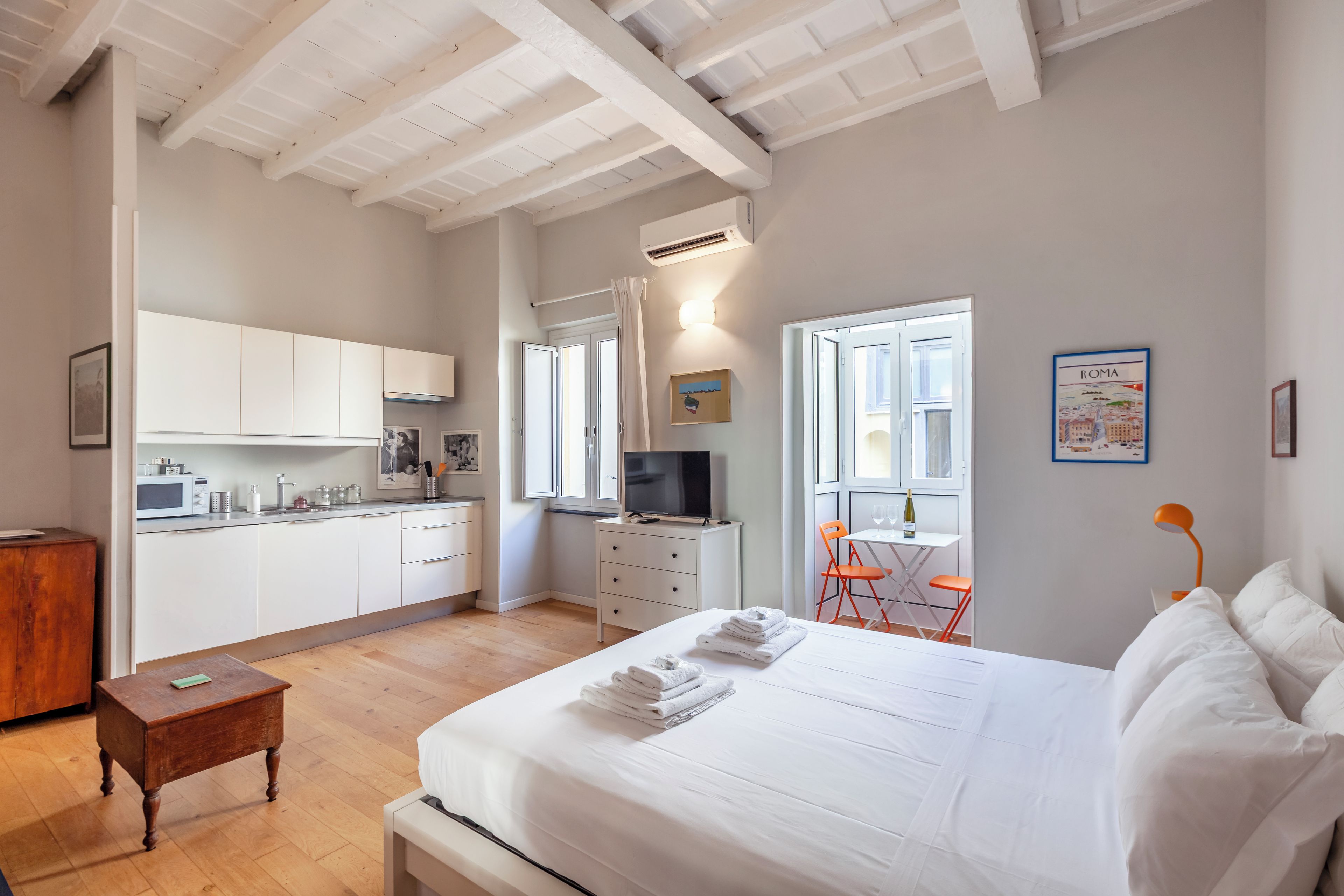 A hotel room with a bed, a desk, a kitchenette, and a bathroom.