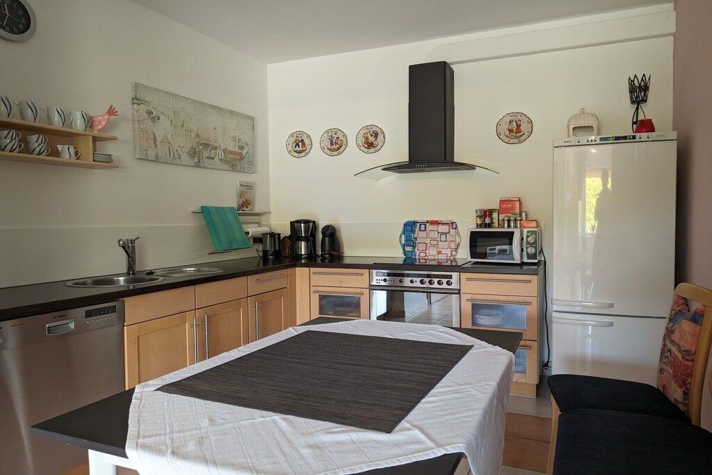 A compact kitchen with a stove, oven, microwave, and refrigerator. There is a dining table with a white tablecloth and a chair.