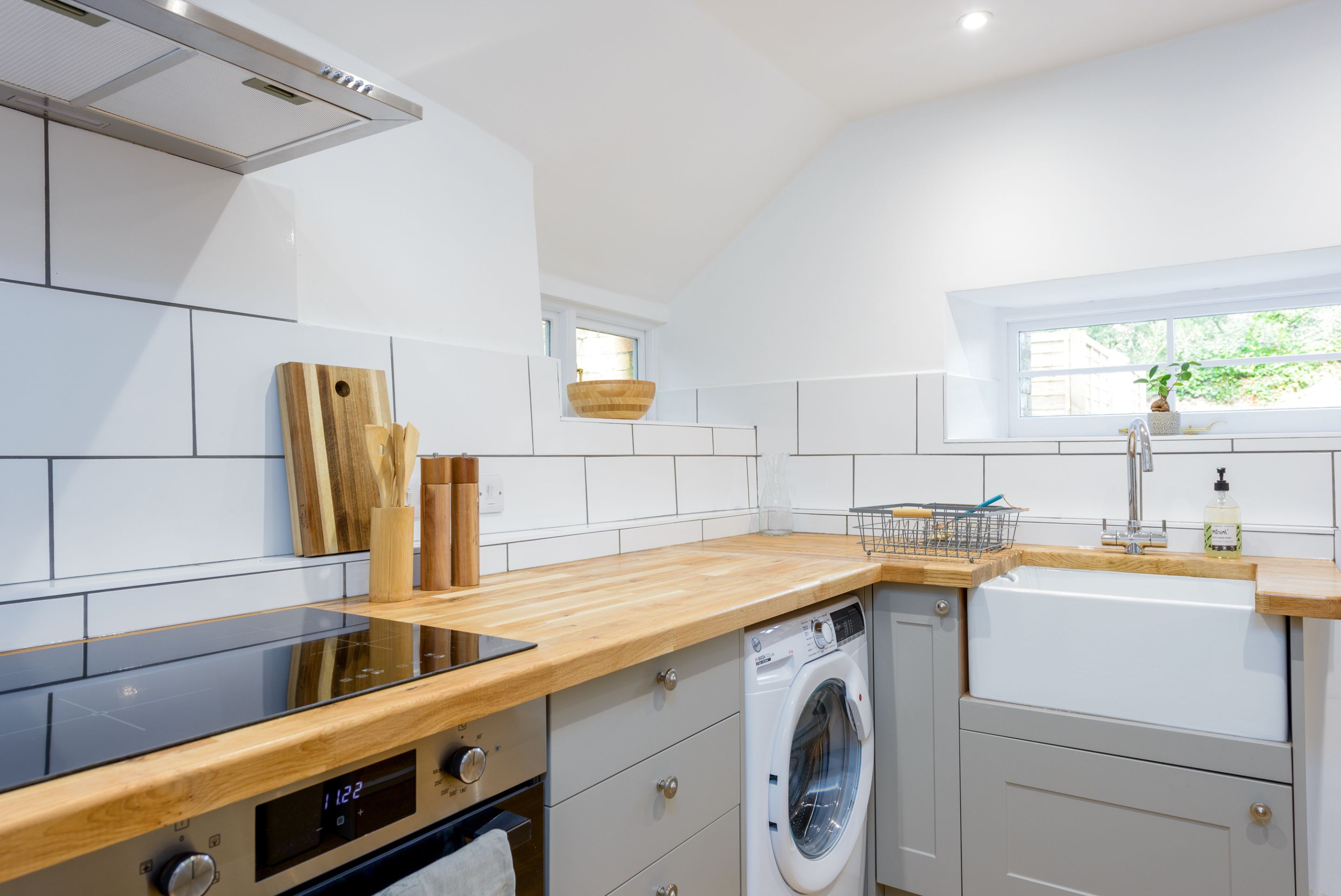 A modern kitchen with a built-in oven, a washing machine, and a window providing natural light.