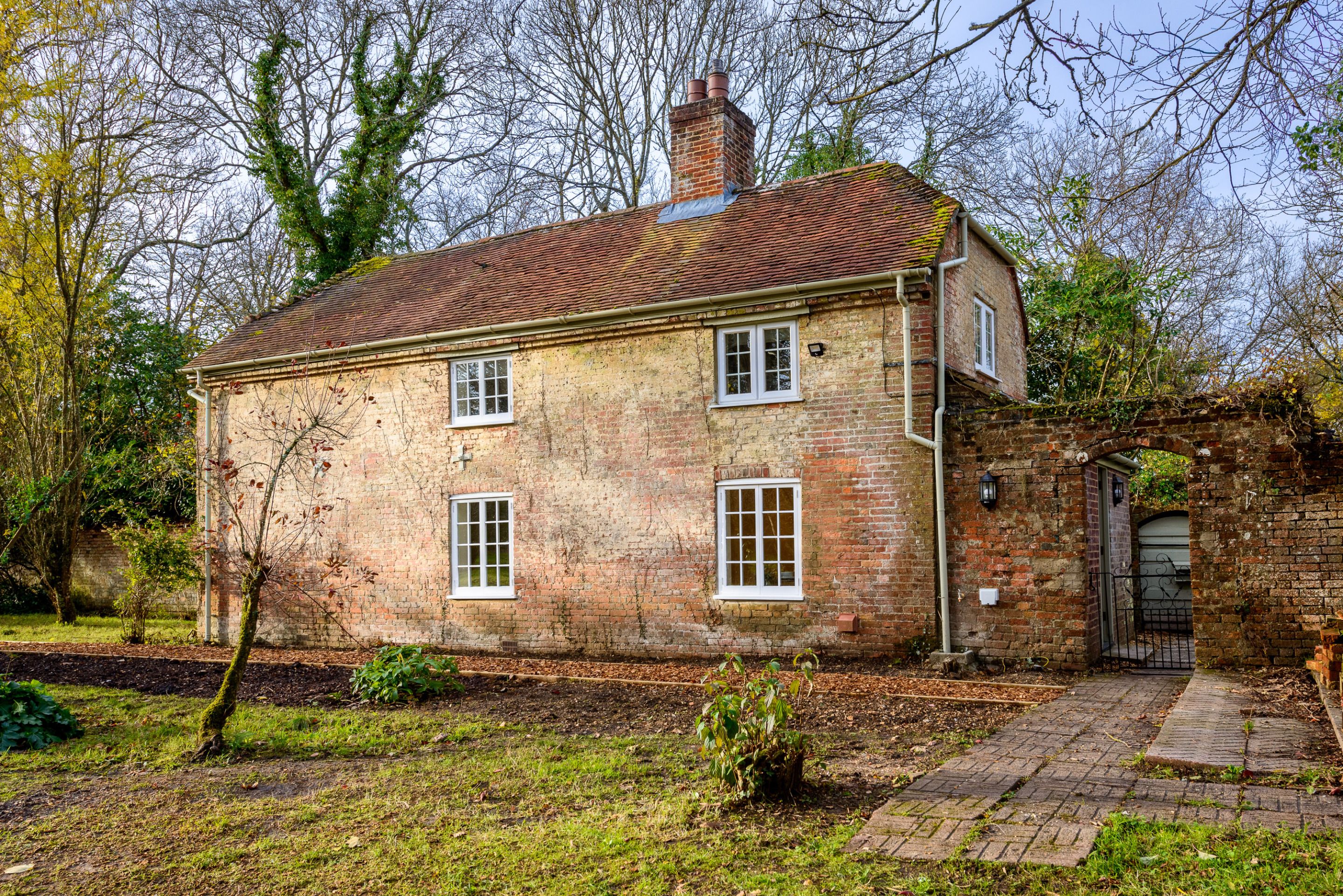 Une maison à deux étages, construite en briques, avec un toit recouvert de tuiles, une cheminée en briques et un petit jardin agrémenté d’un sentier menant à l’entrée.