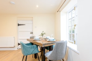 Un coin repas avec une table en bois dressée pour quatre personnes, des chaises de couleur turquoise et une fenêtre donnant sur un paysage agréable.