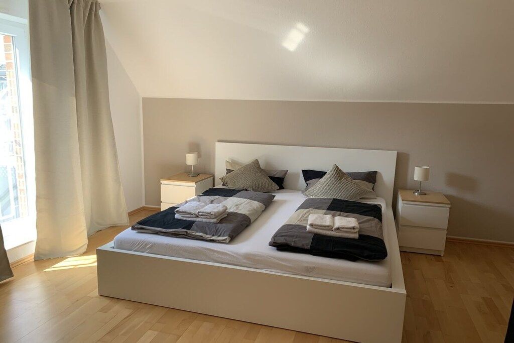 Una cama doble con cabecera, dos mesitas de noche y una ventana con cortinas.