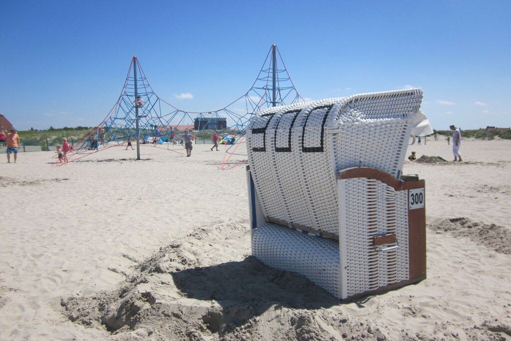 A beach with a large white chair marked with the number 300, a fishing net structure, and people in the background.
