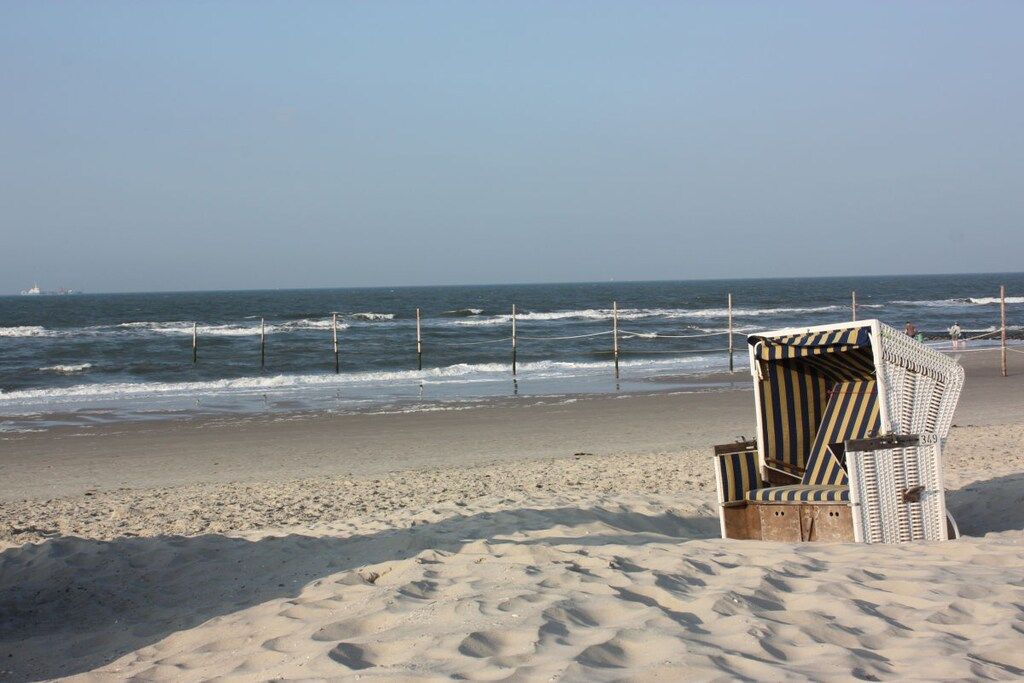 Een strand met een enkele gestreepte ligstoel en een hek.