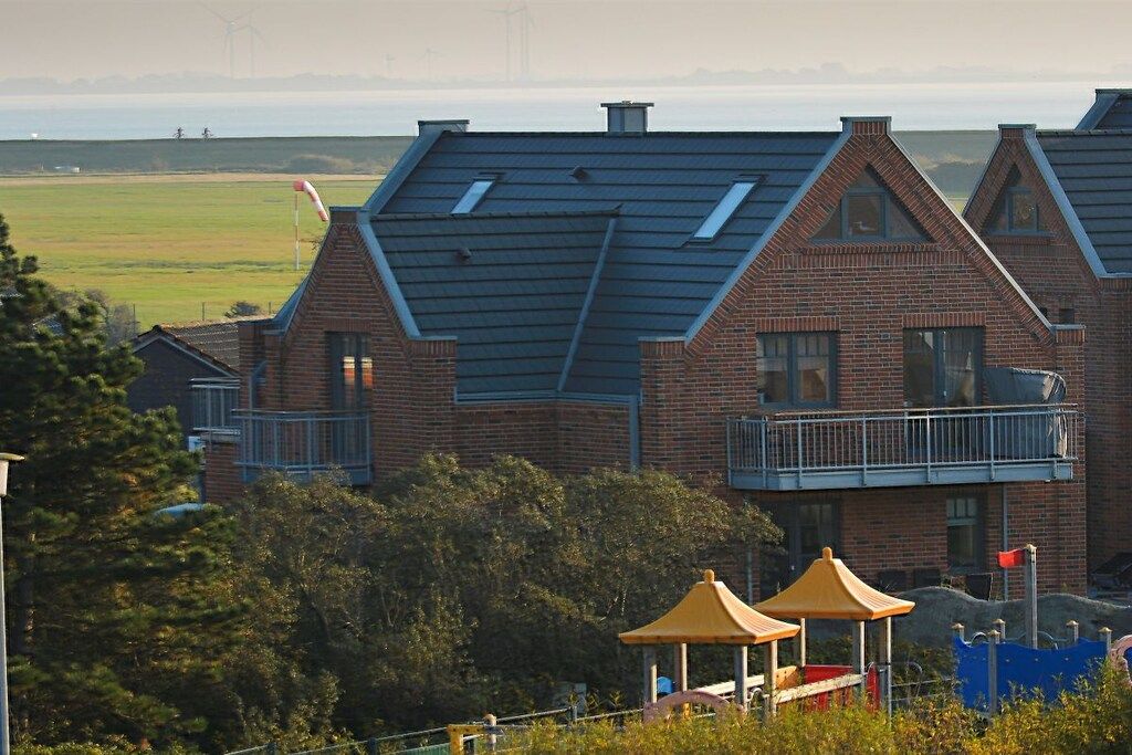 A residential building with a sloped roof, brick exterior, and a balcony with a railing.