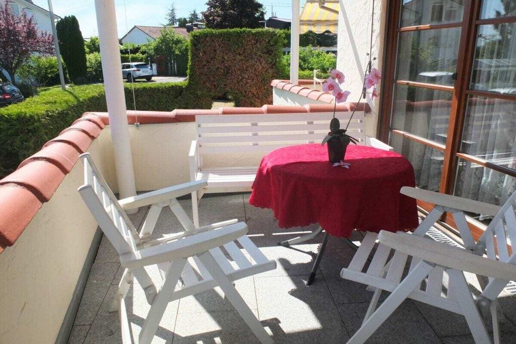 Une terrasse avec des chaises blanches et une table recouverte d’une nappe rouge.