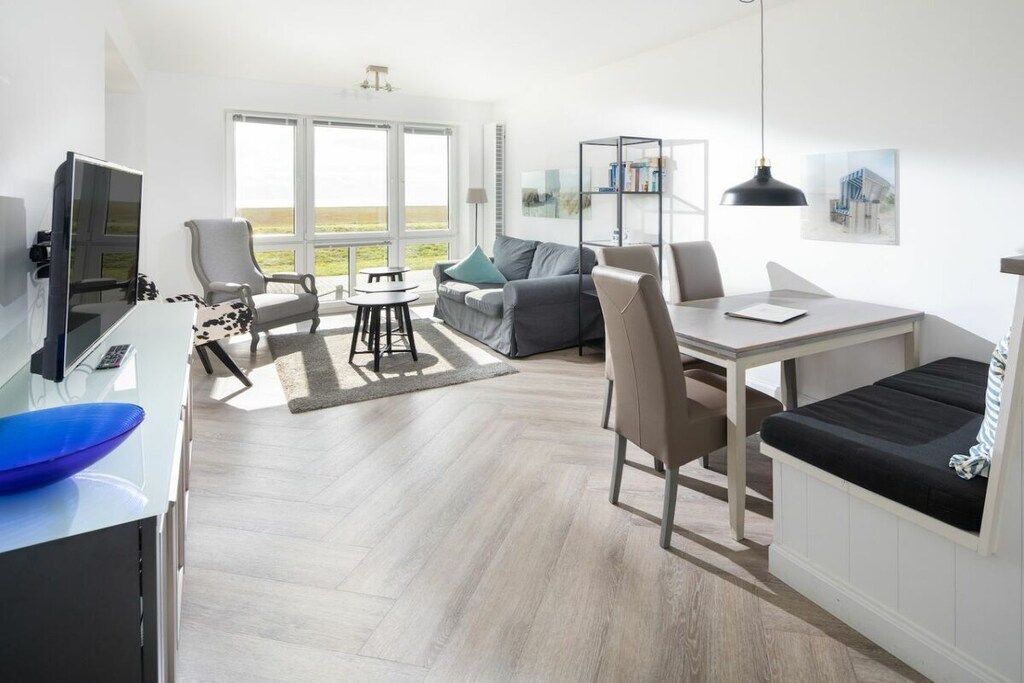 Un salon moderne doté d’un téléviseur à écran plat, d’un coin salon avec un canapé et des fauteuils, d’une table à manger avec des chaises et d’une grande fenêtre offrant une vue panoramique.