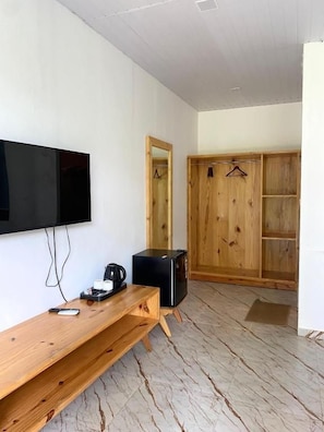 Una habitación con un escritorio de madera, un televisor de pantalla plana, un electrodoméstico pequeño negro y un armario de madera.