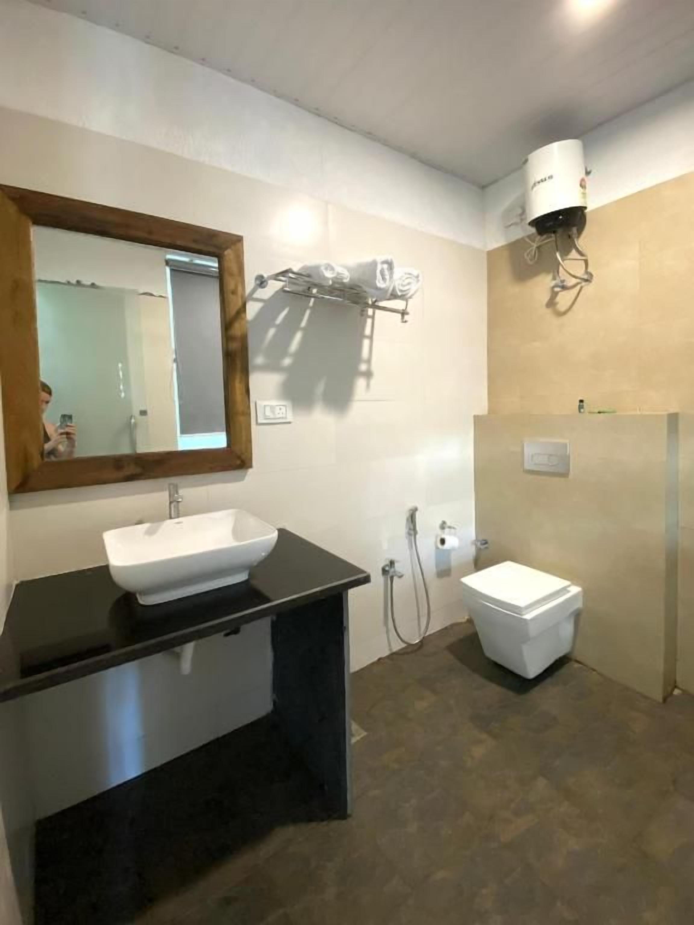 A bathroom with a black countertop sink, a white toilet, a mirror, and a towel rack.